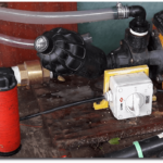 Photo of pipe leading into a brass non-return valve, then a filter, then the pump. Red filter element has been removed.